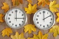 Two clocks, one shows three o\'clock, the other shows two o\'clock. Yellow fallen autumn leaves lie around. Royalty Free Stock Photo