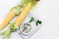 Two cobs of fresh corn and bowl of sauce on white plate