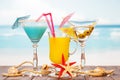 Two cocktails, glass juice, starfish and shells on sea background. Royalty Free Stock Photo