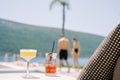 Two cocktails in glasses standing on a table near a sun lounger on the beach against the backdrop of walking man and Royalty Free Stock Photo
