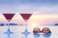 Two cocktails and sunglasses on a table of luxurious tropical beach resort restaurant with beautiful sunset in the background Royalty Free Stock Photo