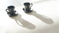 Two Coffee clay black cups on table with bright backlight which draws long cup shadows. Coffee for couple in modern kitchen