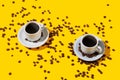 Two coffee cup over a bright yellow color background and many beans spilled Royalty Free Stock Photo