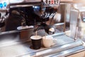 Two coffee cups on coffee device machine, black and white ceramic mugs, process of making hot beverage in eatery, two drinks on Royalty Free Stock Photo