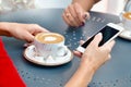 Two coffee cups and hands of young women with smartphone at outdoor cafe