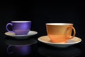 Two coffee cups, orange and purple ceramic, on black background Royalty Free Stock Photo