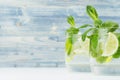 Two cold glasses with tropical cocktail mojito and straw on soft shabby blue and white wood board, copy space, closeup .