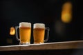 Two cold mugs with beer, with overflowing foam, on wooden table and dark background, space for writing Royalty Free Stock Photo