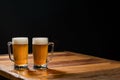 Two cold mugs with beer, with overflowing foam, on wooden table and dark background, space for writing Royalty Free Stock Photo