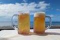 Two cold tankards with beer on the table on the seashore Royalty Free Stock Photo