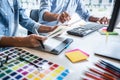 Two colleague creative graphic designer working on color selection and color swatches, drawing on graphics tablet at workplace