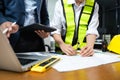 Two colleagues discussing data working and tablet, laptop with architectural project at construction site at desk Royalty Free Stock Photo