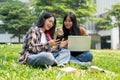 Two college students are sitting on grass in a park, discussing something on a smartphone together Royalty Free Stock Photo