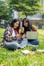 Two college students are sitting on grass in a park, discussing something on a smartphone together Royalty Free Stock Photo