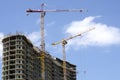 Two colored high-altitude cranes on the background of the cloudy sky and the building under construction Royalty Free Stock Photo