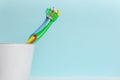 Two colorful kids toothbrushes in white cup on cyan color background. Space for text. Dental care concept