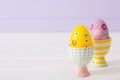 Two colorful painted Easter eggs in vibrant modern egg stands on pastel lilac background