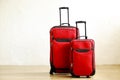 Two colorful red suitcases of same kind different size with telescopic handle up on wooden floor, white wall background. Family tr Royalty Free Stock Photo