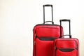 Two colorful red suitcases of same kind different size with telescopic handle up on wooden floor, white wall background. Family tr Royalty Free Stock Photo