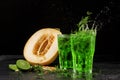 Two colorful splashing tarragon cocktails on a black background. Green tarragon, cut sweet melon, and sour lime. Royalty Free Stock Photo