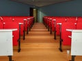 Two columns of amphitheater lecture university or conference big room rows of red chairs and white tables aligned with path in