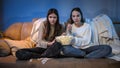 Two concentrated girls watching TV on sofa and eating popcorn from big bowl Royalty Free Stock Photo