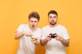 Two concentrated young men playing a video game with gamepads in their hands a blue background. Two friends with joysticks in Royalty Free Stock Photo