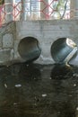 Two concrete sewer pipe covered under bridge. Black dirty water Royalty Free Stock Photo