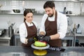 Two confectioners, a man and a woman, decorate a mousse cake with a mirror glaze with handmade chocolates