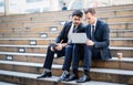 Two confident business men sitting on stairs looking at laptop in urban city Royalty Free Stock Photo