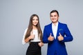 Two confident smiling businesspeople in formalwear showing thumbs-up on gray background Royalty Free Stock Photo