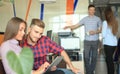 Two confident young people looking at touchpad while their colleagues working in the background.