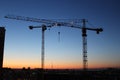 Two construction cranes with gradient sunset sky