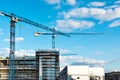 Two construction tower cranes at a construction site against a blue sky with clouds. Modern high-rise office building under Royalty Free Stock Photo