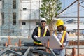 Two construction worker looking at a floor plan, standing in front of a large building site with helmet and safety gear. Day time Royalty Free Stock Photo