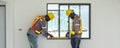Two construction workers in safety gear carefully evaluate a window installation using a level tool inside a building. The setting Royalty Free Stock Photo