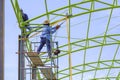 Two construction workers on scaffolding are repairing green metal roof structure of warehouse building against blue sky Royalty Free Stock Photo