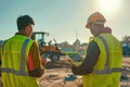 Two construction workers standing on-site, wearing high-visibility safety vests under bright sunlight Royalty Free Stock Photo
