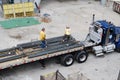 Two construction workers working on a flatbed truck at a building project site.