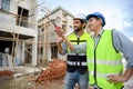 Two constructions man in vests with helmets working on under-construction building site. Engineer foreman discusses with a Royalty Free Stock Photo