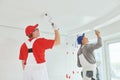 Two painter workers with roller painting ceiling surface into white