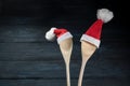 Two cooking spoons with red Santa Claus hats against a dark blue wooden background, Christmas invitation for a dinner or greeting Royalty Free Stock Photo