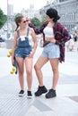 Two cool women smiling and looking to each other with a skateboard. Royalty Free Stock Photo