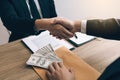 Two corporate businessmen shaking hands while one man places money on envelope document in office room with corruption concept Royalty Free Stock Photo