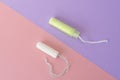 Two cotton tampons with light green applicator and without applicator on a pink and violet background. Hygienic types of tampons.