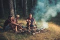 Two couples camping in woods. Cooking sausages on campfire. Warm summer evening in forest