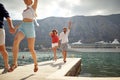 Two couples holding hands running on pier by sea. Cruiser, city and mountains in background. Summertime holiday. Fun, togetherness Royalty Free Stock Photo