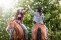 Two cowgirl friends with horses facing the opposite direction give a high five Royalty Free Stock Photo