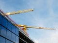 Two cranes against blue cloudy sky and part of a modern building at glass installation phase. New modern architecture style. New Royalty Free Stock Photo