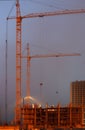 Two cranes on the construction site, unfinished house, foggy evening, building lighting on twilight